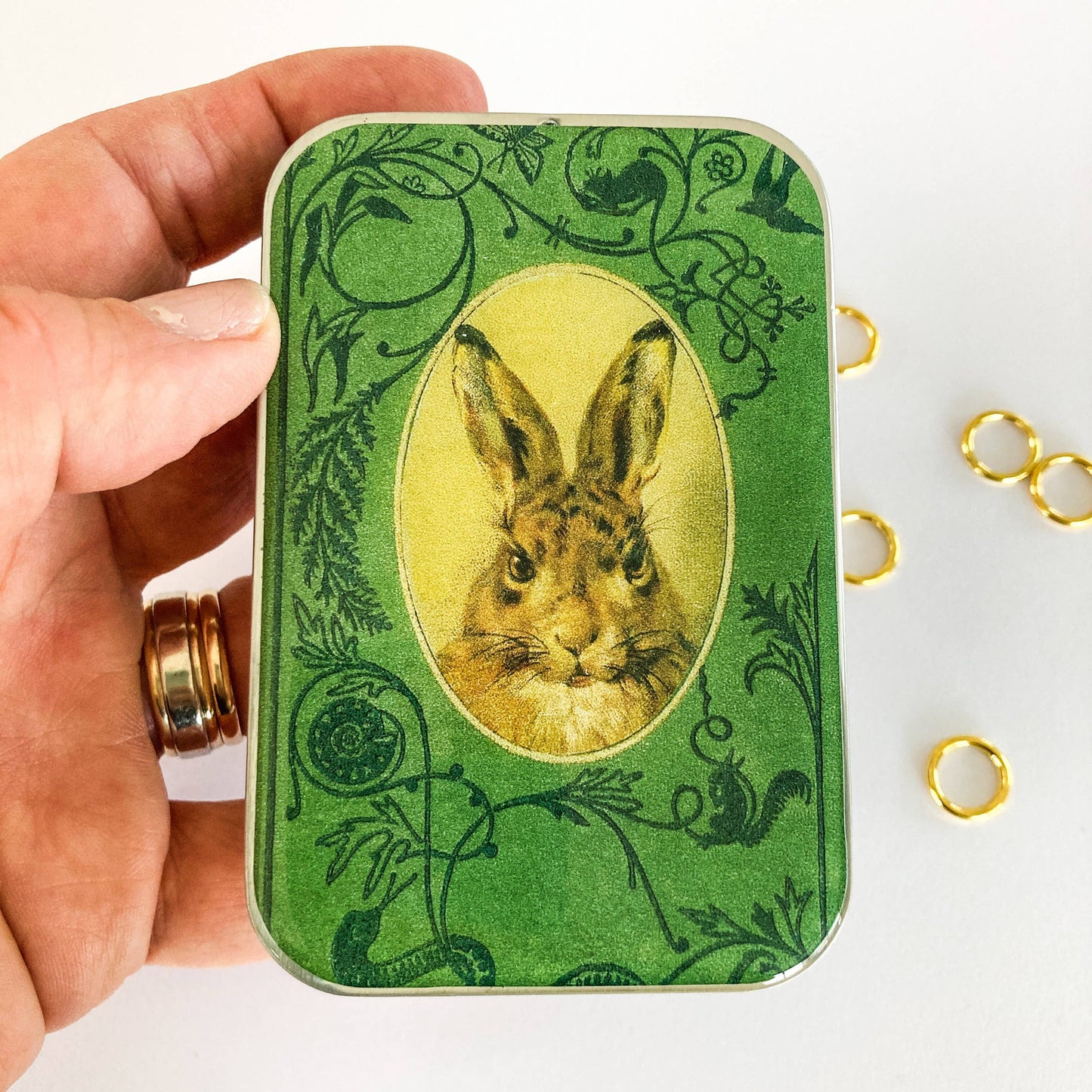 Hand holding a green tin with a rabbit illustration on a white background