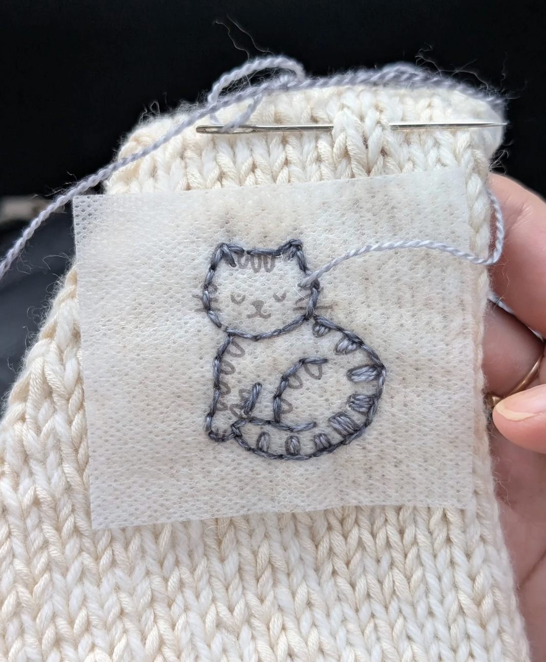 Embroidered cat design on a knitted sleeve.