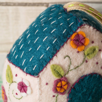 Felted fabric item with floral patterns and blue roof on a neutral background