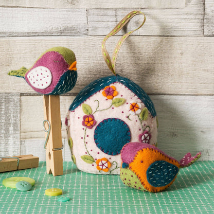 Colorful bird-shaped felt ornament on a wooden surface with a checkered tablecloth.