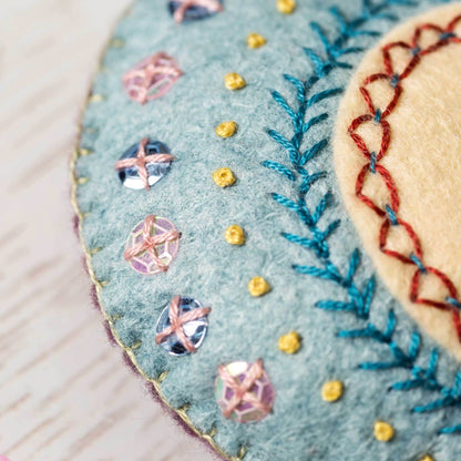 Close-up of embroidered felt pieces with sequins and thread details on a light background