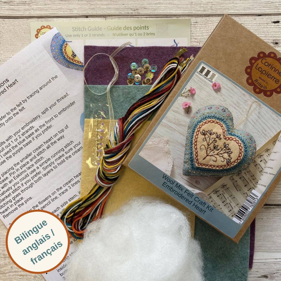 Embroidery kit with heart-shaped fabric piece, thread, and instructions on a wooden surface.