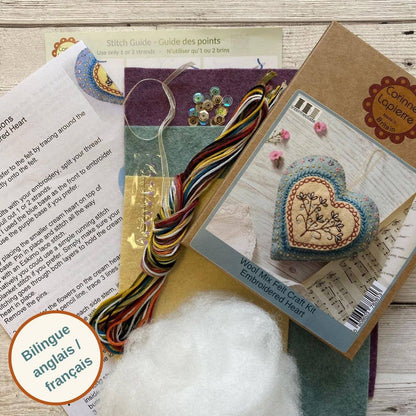 Embroidery kit with heart-shaped fabric piece, thread, and instructions on a wooden surface.