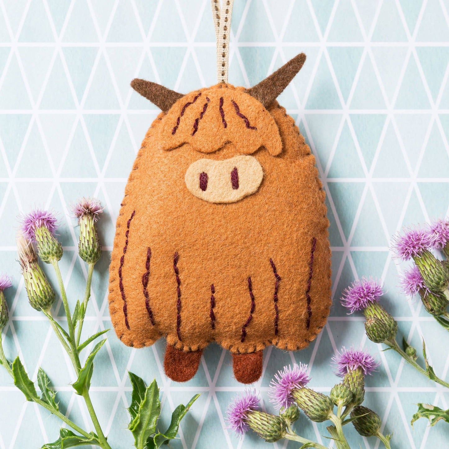 Felt Highland cow ornament with thistle flowers on a geometric patterned background