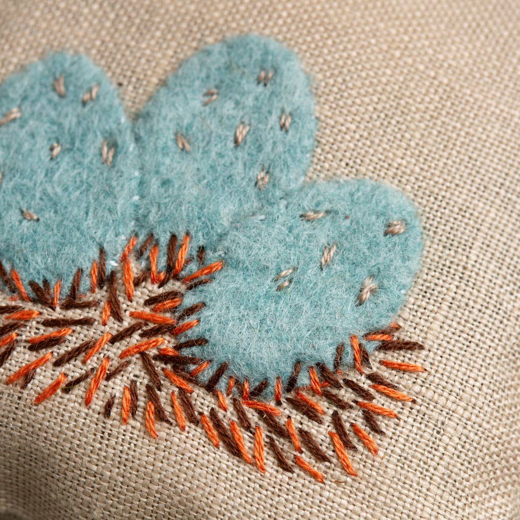 Embroidered bluebird eggs with orange and brown nest on a beige fabric background