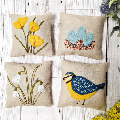 Set of four embroidered pillows with floral, bird, and nature-themed designs on a wooden surface.