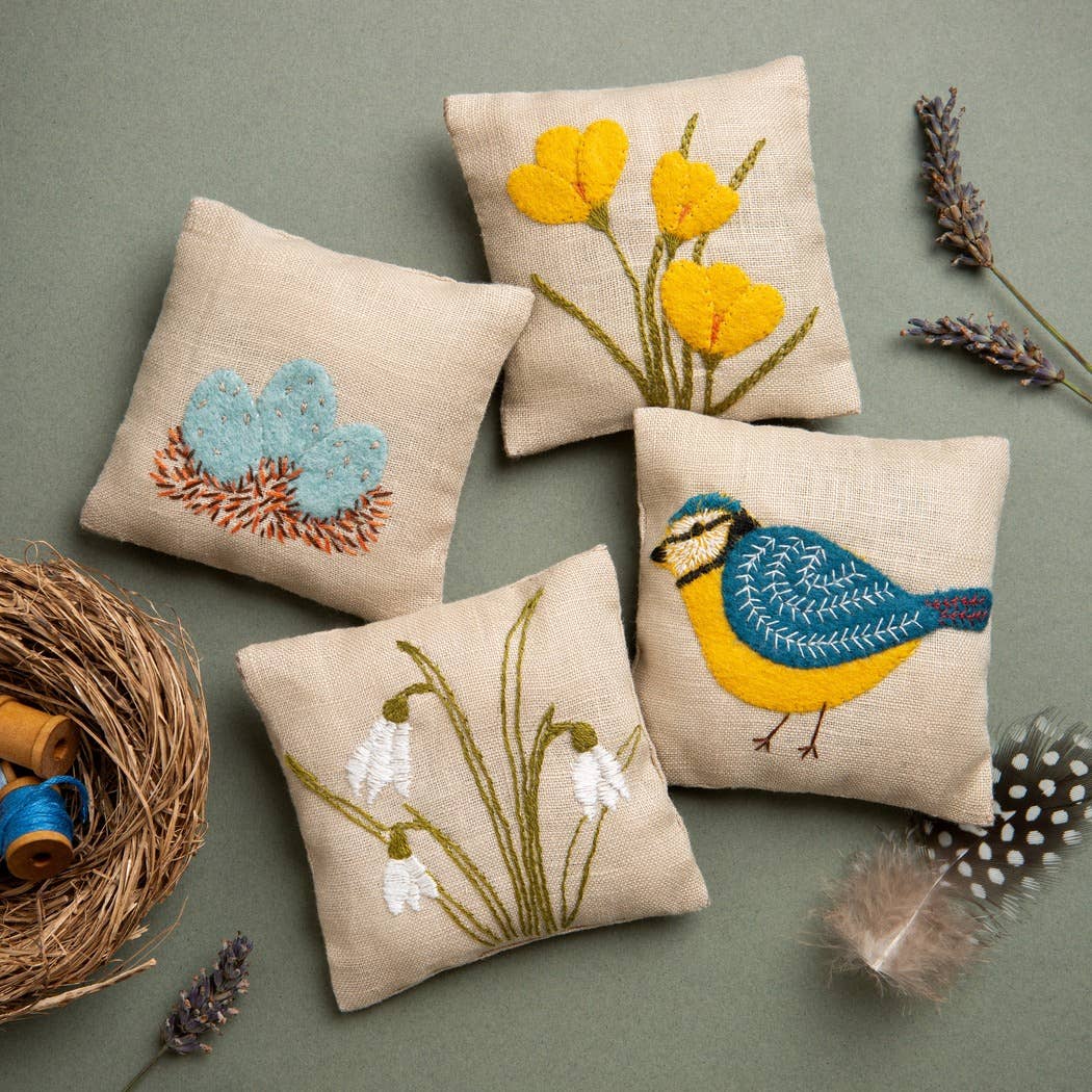 Four embroidered linen lavendar pillows with floral and bird designs on a green background