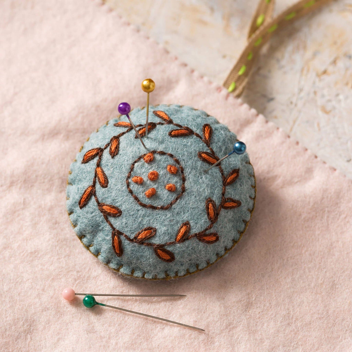 Felted pincushion with embroidered design on a soft pink background