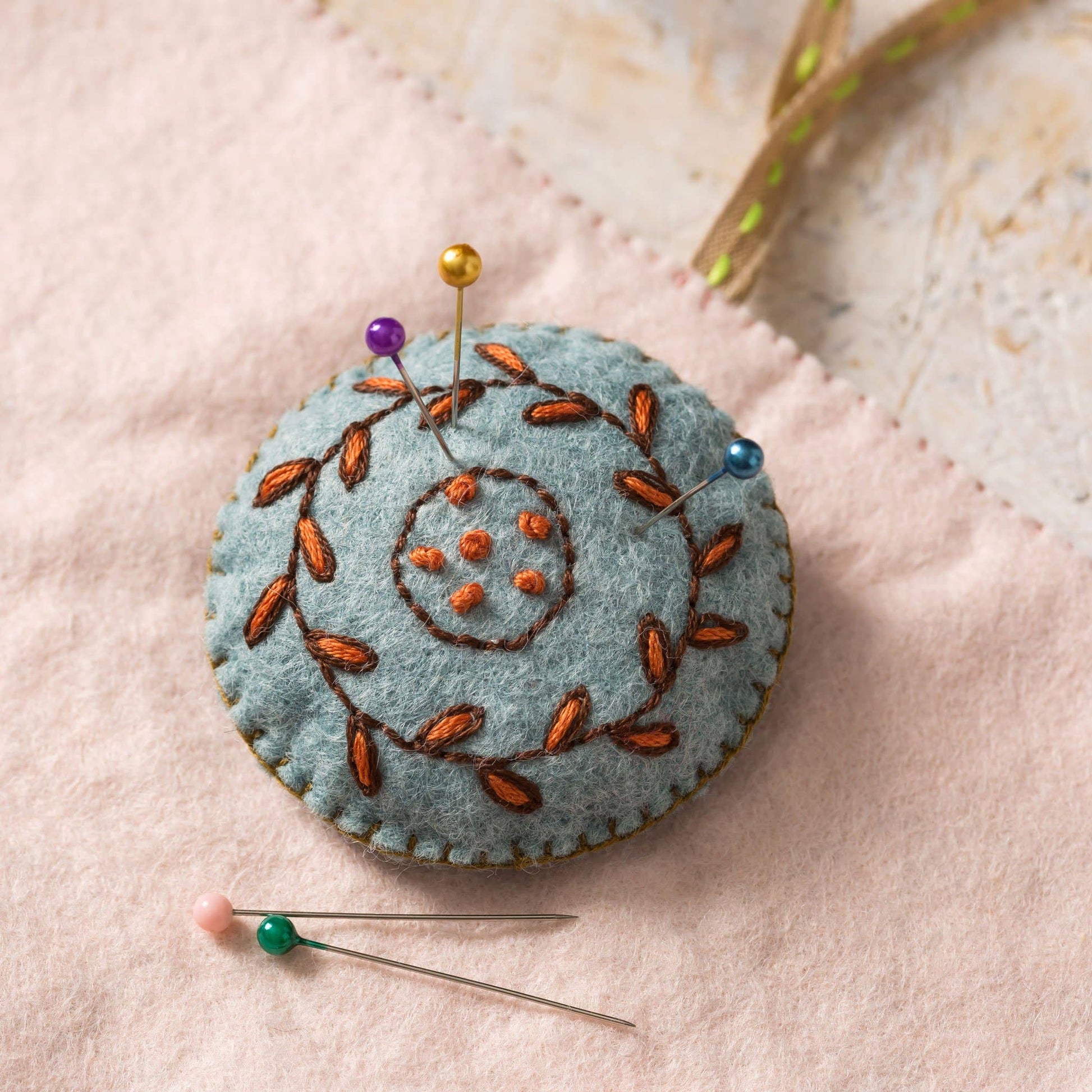 Felted pincushion with embroidered design on a soft pink background