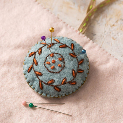 Felted pincushion with embroidered design on a soft pink background