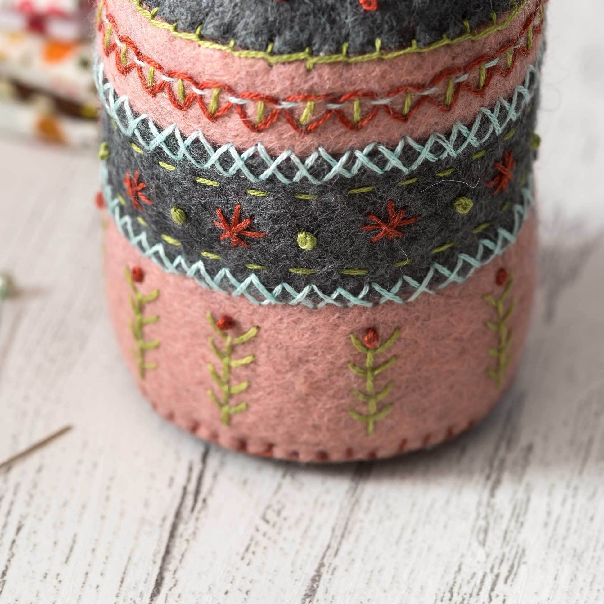 Decorative felt pin cushion with embroidered patterns on a wooden surface