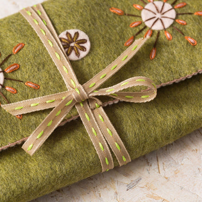 Green fabric with embroidered flowers and a ribbon on a light background