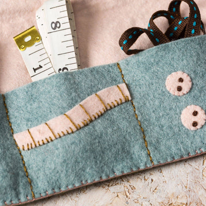Felt pouch with buttondesign, ribbon, and measuring tape on a light background