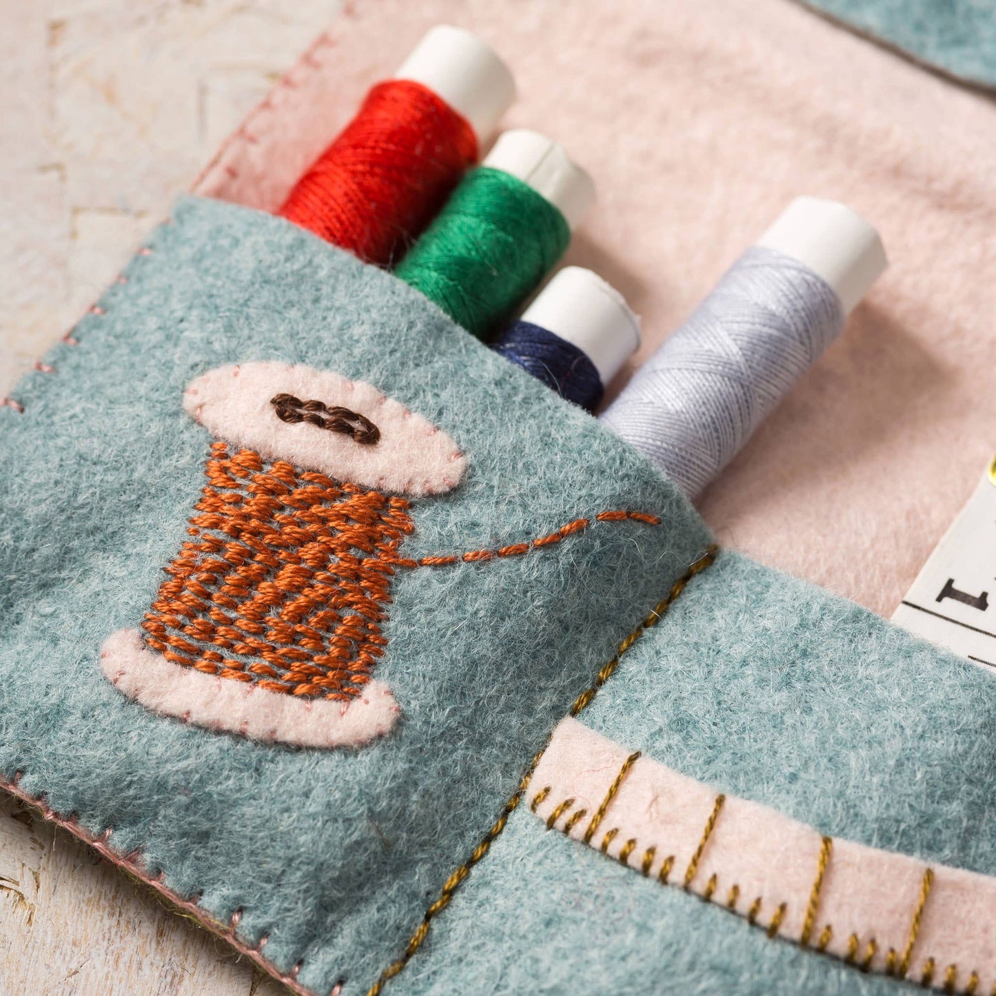 Felt thread holder with embroidered spool of thread design on a wooden surface.