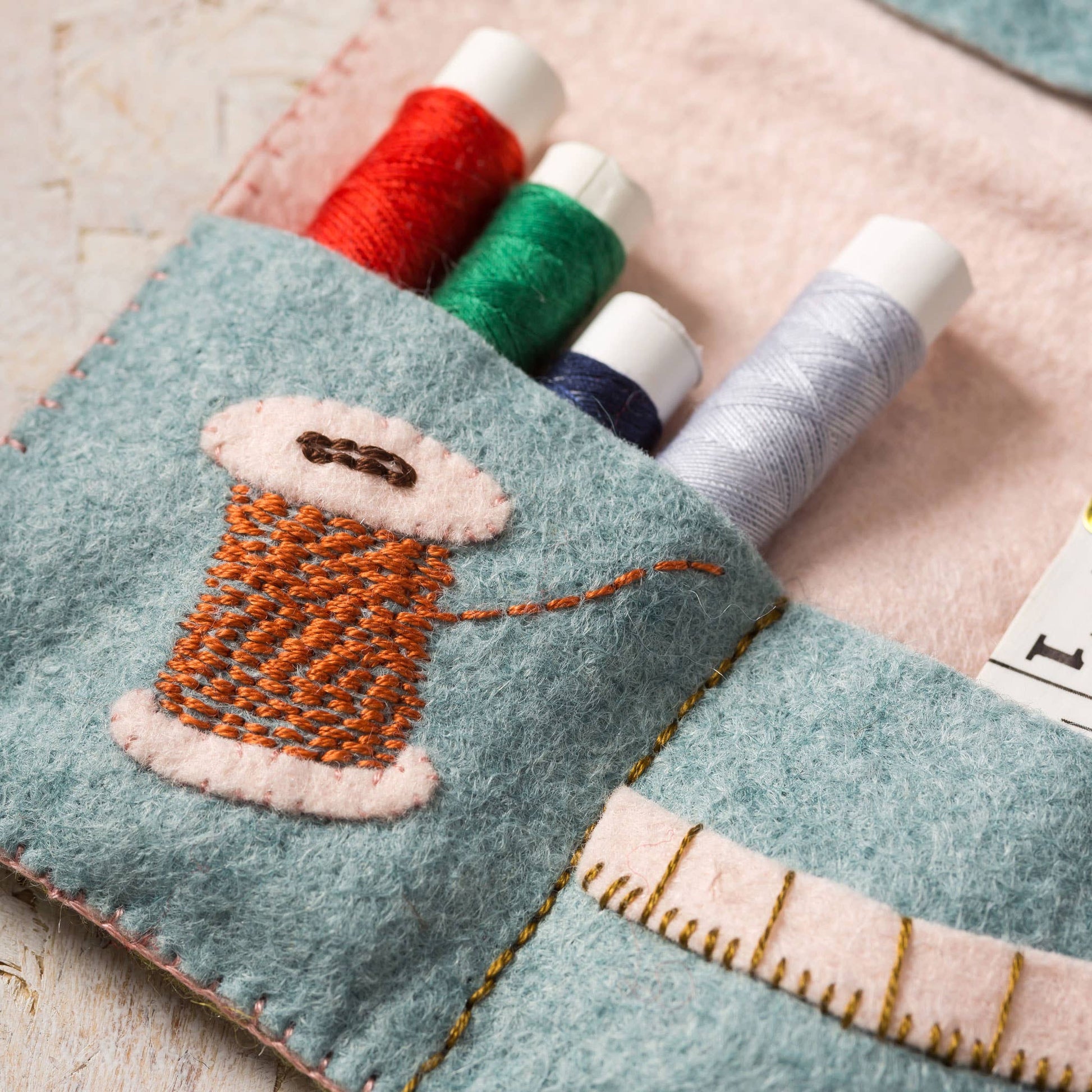 Felt thread holder with embroidered spool of thread design on a wooden surface.