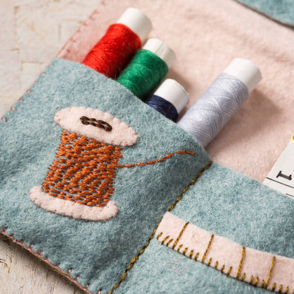Felt thread holder with embroidered spool of thread design on a wooden surface.
