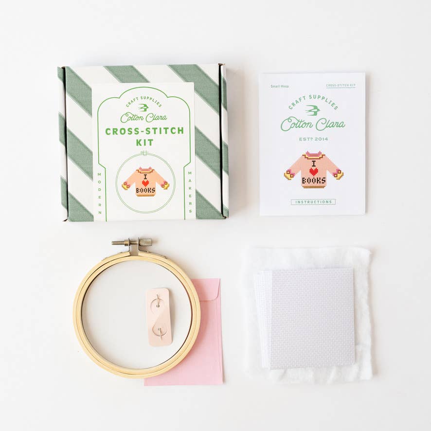 Cross-stitch kit with hoop, fabric, and packaging on a white background