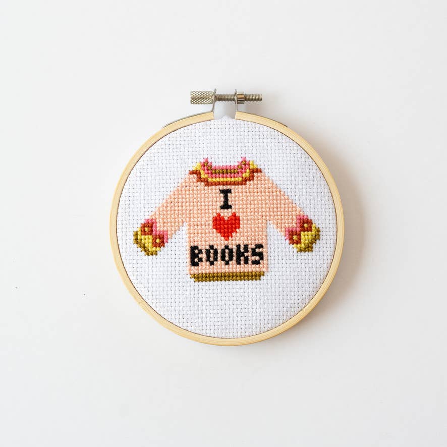 Cross-stitched design of a sweater with 'I love books' text in a wooden hoop on a white background