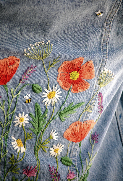 Embroidered floral design on denim fabric with flowers and bees.