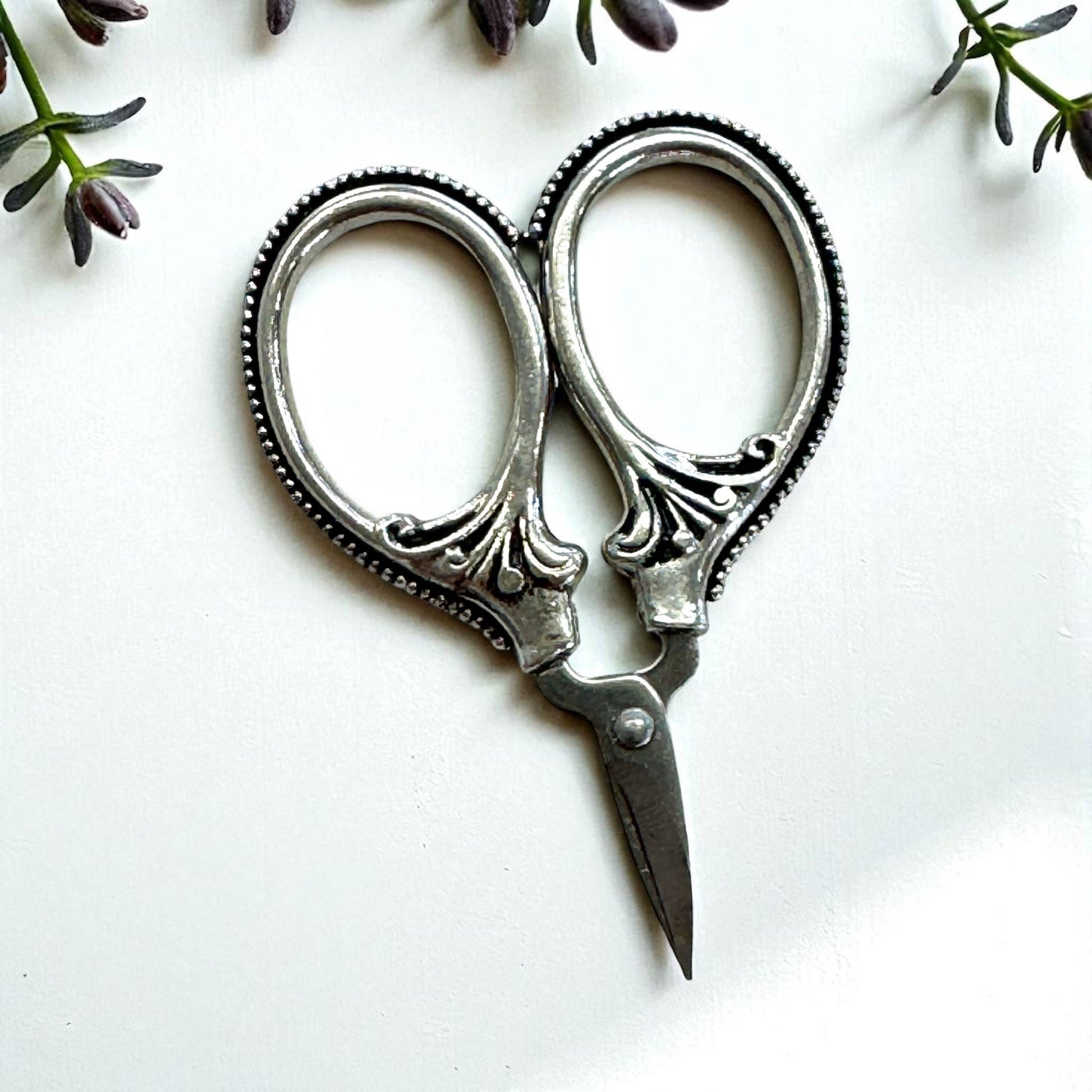 Decorative silver scissors on a white background with green leaves