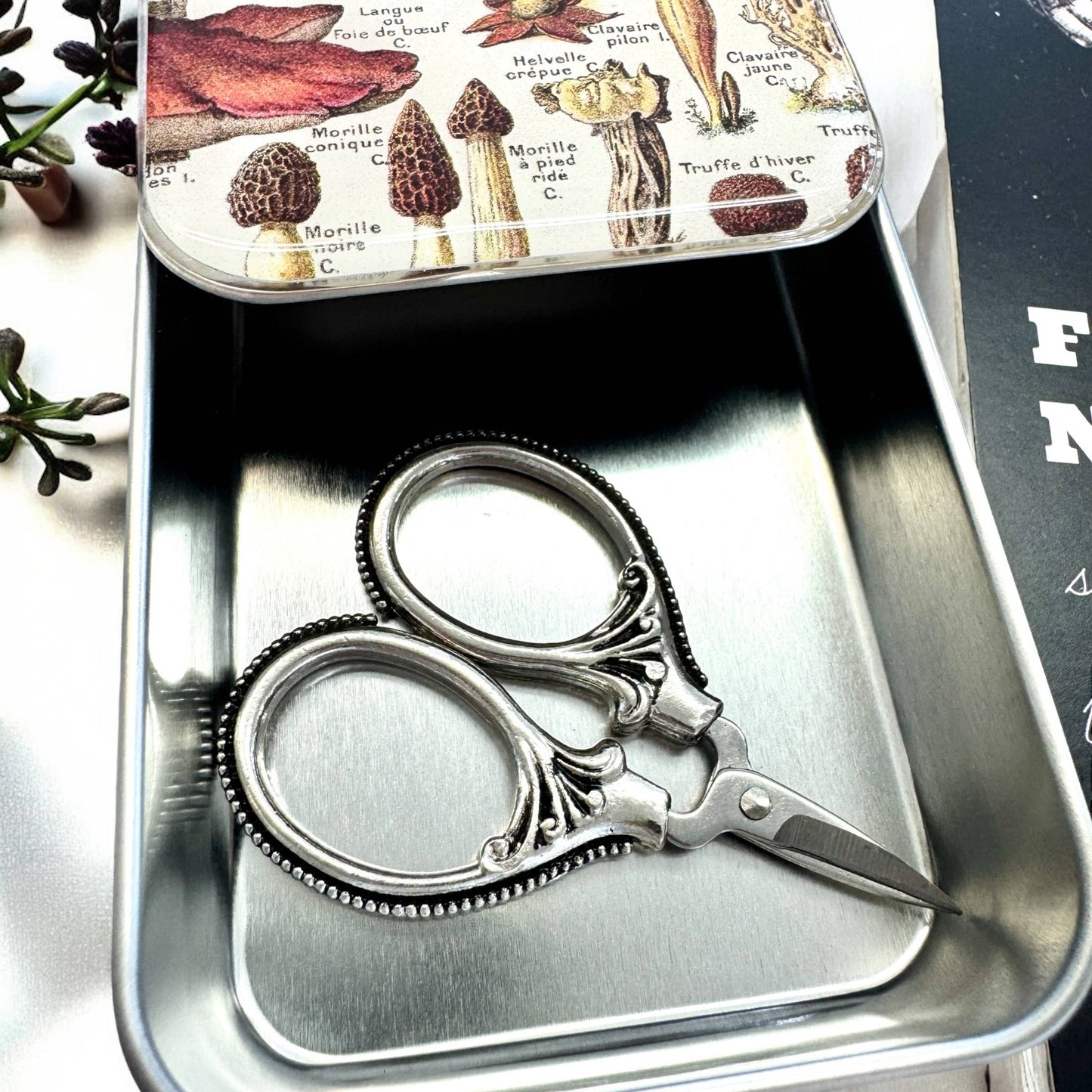 Decorative scissors in a metal tin with a mushroom-themed lid.