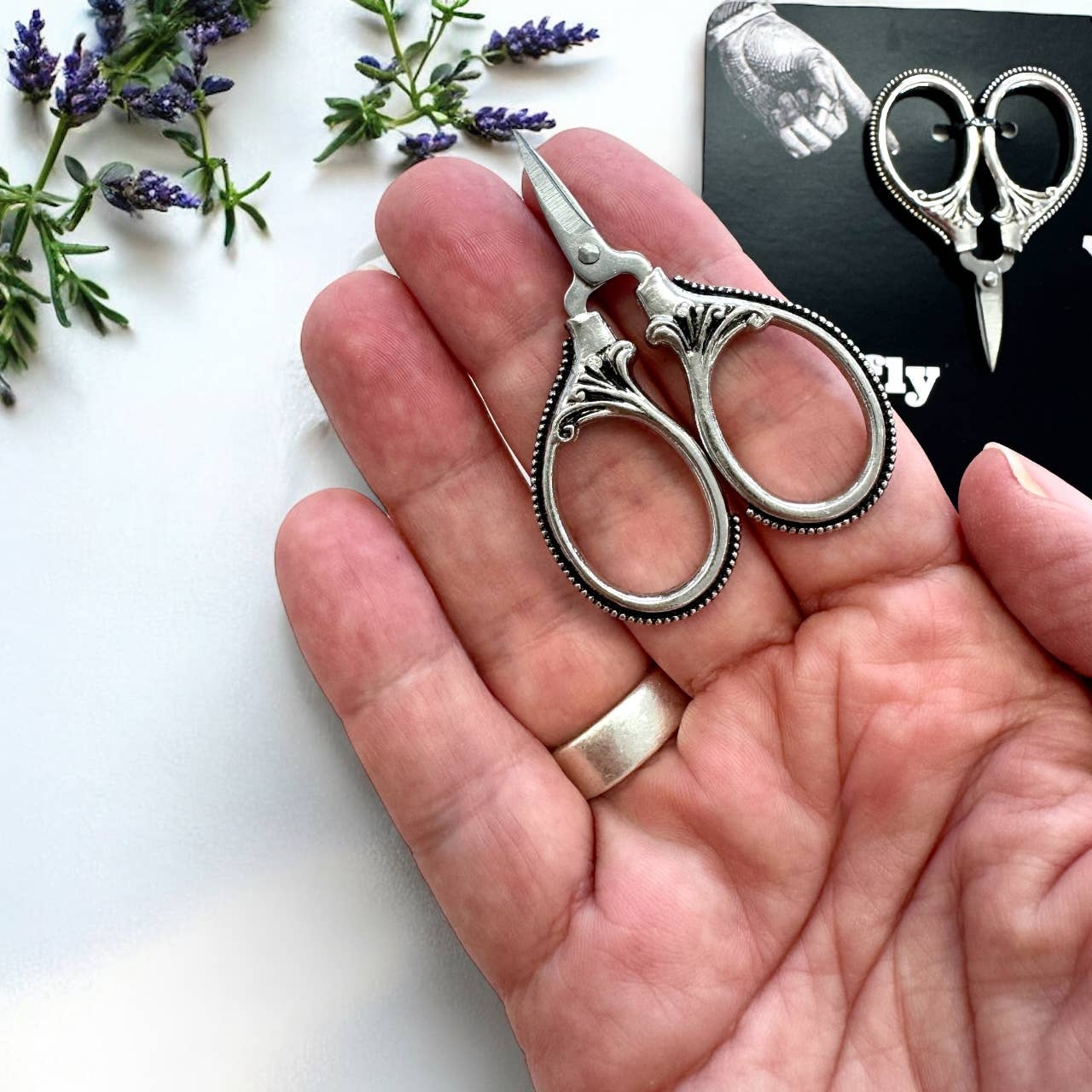 Decorative scissors held in a hand with lavender flowers in the background