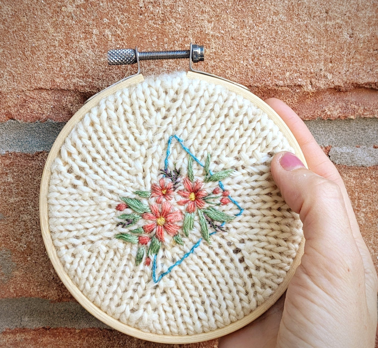 Embroidery hoop with floral design held by a hand on a textured surface