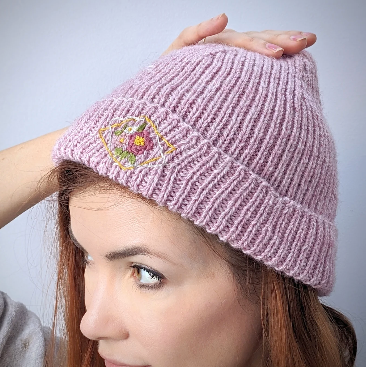 Pink knitted beanie with embroidery held by a person against a plain background