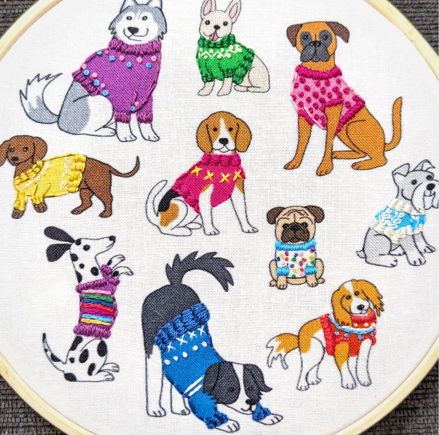 Embroidery hoop with a pattern of dogs wearing colorful sweaters.