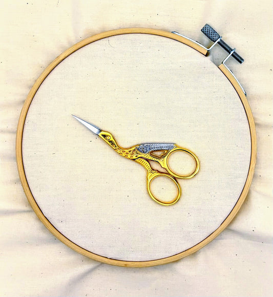 Gold stork scissors on a wooden embroidery hoop with white fabric background