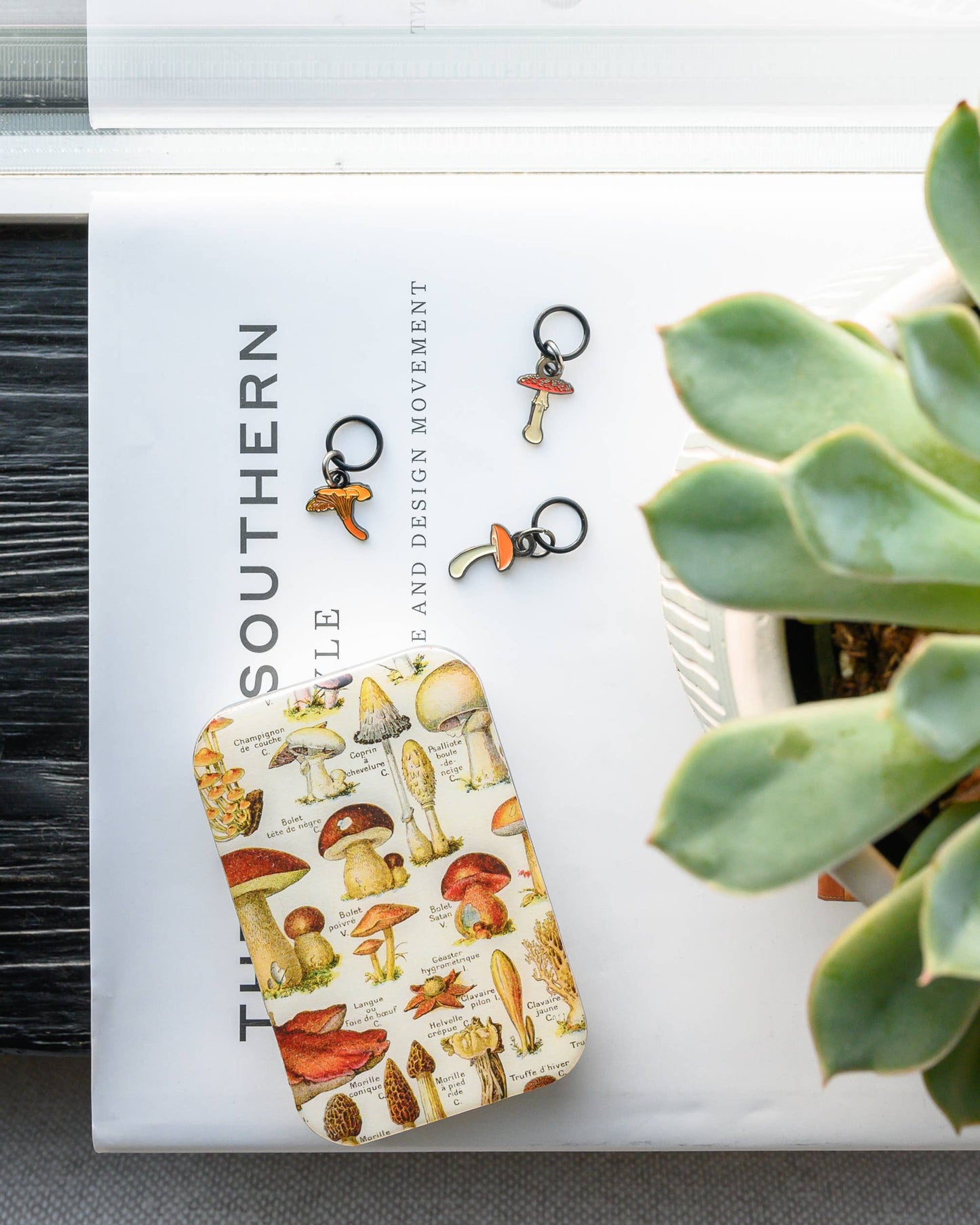 Tin with a mushroom design on a surface with a plant and book in the background