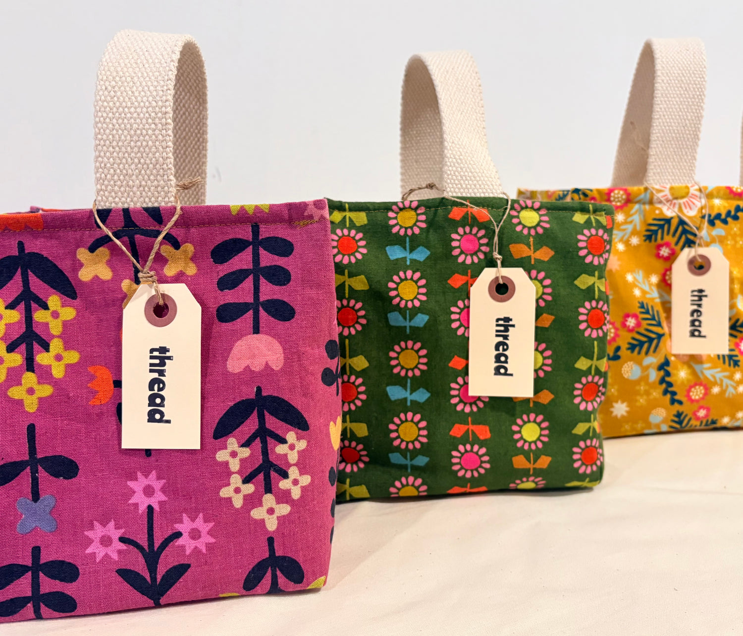 Three fabric bags with floral patterns and 'thread' tags on a light background